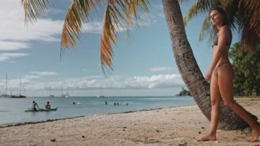 Genç bir kadın kumlu bir plajda yürürken bir anlık rahatlığın tadını çıkarıyor, batan güneş sahneye sıcak bir ışık saçıyor.