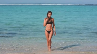 Genç bir kadın, kristal berrak sular ve parlak bir güneşin altındaki beyaz kumlarla çevrili tropikal bir plajda rahatça geziniyor. Mutlu ve kaygısız görünüyor. Doğanın tadını çıkarıyor. Özgürlük ve rahatlama.
