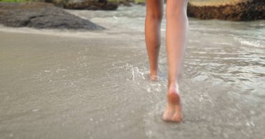Kadın ayakları çıplak ayakla kumsalda yürüyor, deniz suyu sıçratıyor. İnce kadın ayakları akşam ışığında deniz kıyısında sörf yapıyor. Yaz tatilindeki kız turist, tropik ada beldesinde. Yavaş, arka plan