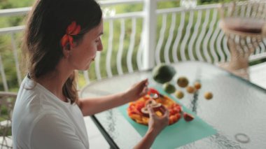 Turist, yemyeşil manzaralı bir balkonda tropikal bir kahvaltı yapıyor. Bir tabak taze papaya ve diğer egzotik meyvelerin tadını çıkarıyor, canlı ve iştah açıcı bir sahne yaratıyor.