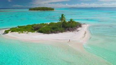 Maldivler 'deki bir turkuaz gölün ortasında, küçük ıssız bir adanın beyaz kumlu sahilinde yürüyen genç bir kadının hava görüntüsü...