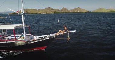 Endonezya 'daki güzel Komodo Ulusal Parkı' nda yelken açan bir yatın pervazında güneşlenen genç bir turistin hava aracı görüntüleri.