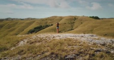 Endonezya 'nın Sumba kentindeki yuvarlanan tepelerin ve savananın nefes kesici manzarasını kucaklayan, kolları açık, kaygısız kadın turist.