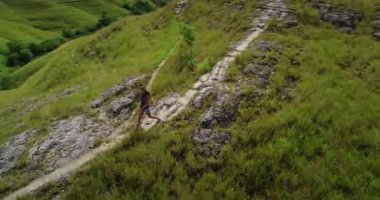 Genç bir kadın güzel yeşil bir vadide yürüyüş yapıyor güneşli bir günde manzarayı keşfediyor, sürdürülebilir ve sorumlu turizmi destekliyor.