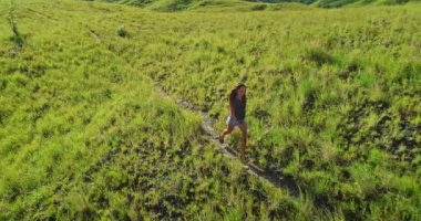 Genç kadın yemyeşil tepelerde yürüyor, doğanın sonsuzluğundan zevk alıyor ve dramatik, bulutlu gökyüzünün altında açık alan özgürlüğünü kucaklıyor.