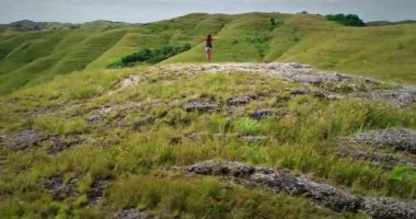 Kollarını açmış, Endonezya 'nın Sumba Adası' ndaki yemyeşil bir tepenin zirvesinden çarpıcı panoramik manzarayı kucaklayan kadın turist.