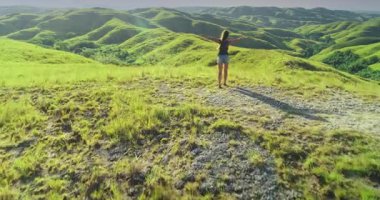 Kadın turist, kollarını açmış Sumba Adaları 'nın güzelliğini kucaklıyor güneşli bir yaz gününde yemyeşil tepeler, doğal güzelliği kutluyor.