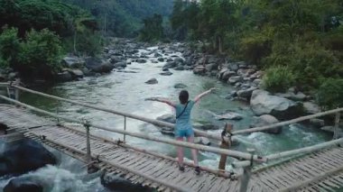 Kırsal ahşap bir köprüde duran insan, kollarını açmış, sakin doğal manzarayı kucaklıyor. Akan nehir ve yemyeşil yeşillik sakin, resim gibi bir manzara yaratır.