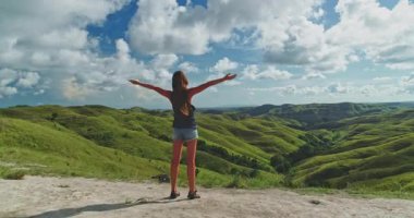 Endonezya 'nın Sumba Adası' ndaki sarmal yeşil tepelerin ve mavi gökyüzünün nefes kesici manzarasını kucaklayan genç bir kadın.