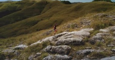 Genç atletik kadın Endonezya, Sumba 'da güzel bir arazide kayalık bir tepeye tırmanıyor güneşli günün tadını çıkarıyor ve vahşi doğayı keşfediyor.