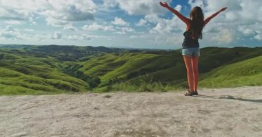 Kollarını açmış genç bir kadın, yuvarlanan yeşil tepelerin ve Endonezya 'da popüler bir turizm merkezi olan Sumba Adası' nın engin manzarasının güzelliğini kucaklıyor.