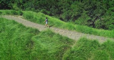 Bali 'nin Ubud kentindeki Campuhan Tepesi Yürüyüşü' nde, yemyeşil bitki örtüsüyle çevrili ve güneşli havanın tadını çıkaran genç bir kadının insansız hava aracı görüntüleri.