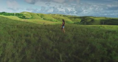 Genç bir kadın, bulutlu bir gökyüzünün altında yuvarlanan tepelerle çevrili yemyeşil bir çayırda yürüyor. Doğanın huzur ve yalnızlığını kucaklıyor. Güzelliği.