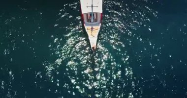 Endonezya 'daki Komodo Ulusal Parkı' nda mavi sularda yüzen yat, arkasında bir uyanış yaratıyor. Güneş, su yüzeyine yansıyor.