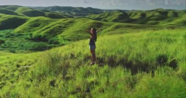 Genç bir kadın açık kollarla yemyeşil bir tepede duruyor. Endonezya 'daki Sumba Adası' nın büyüleyici manzarasını kucaklıyor. Güneşin sıcaklığını ve hafif esintisini hissediyor.