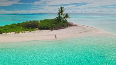Cennet adasında tatilin tadını çıkaran genç bir kadının hava aracı görüntüsü. Beyaz bir kumsalda Maldivler 'deki turkuaz okyanusun kenarında duruyor.