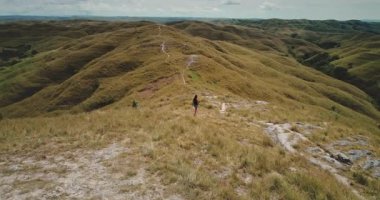 Endonezya 'nın Sumba Adası' ndaki kuru otlarla kaplı yuvarlanan tepelerin ortasında yürüyen bir kadın güneşli bir yaz gününde manzaranın tadını çıkarıyor.