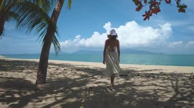 Bir kadın Tayland 'da beyaz bir plajda, turkuaz denize doğru, yaz tatilini kucaklayarak neşeyle yürüyor.