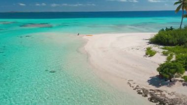 Bir kadının turkuaz su ve sarı bir kanoyla tenha bir plajın sessizliğinin tadını çıkardığı hava manzarası. Görüntü huzur, özgürlük ve doğanın güzelliğini çağrıştırıyor.