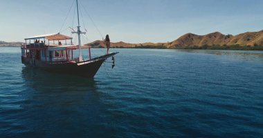 Endonezya 'daki Komodo Ulusal Parkı' nda, güneşli günün ve adaların nefes kesici manzarasının tadını çıkaran genç bir kadınla yat gezintisi.