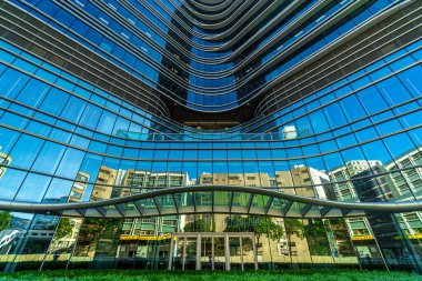 Reflections of old factory and blue sky on a Modern commercial building at low angle view