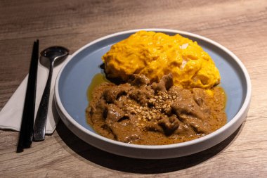 Japanese Style Curry Satay Omurice, Omelette Rice with beef and egg on wooden table with chopstick, spoon, spot lighting