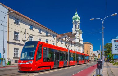Bratislava, Slovakya - 14 Mayıs 2024: Eski binalar ve Macaristan Kilisesi 'nin yanından geçen kırmızı bir modern tramvay
