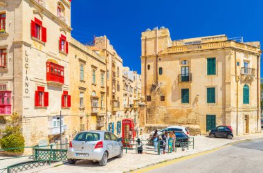 Valletta, Malta - 2 Nisan 2025: Geleneksel mimari, park edilmiş arabalar, Londra kırmızı telefon kulübesi ve bir grup turist ile Valletta 'nın sokak manzarası