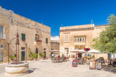 Mdina - 4 Mayıs 2025, Malta: Antik Mdina kentinde bir kafede oturan insanların bulunduğu samimi küçük bir meydanın manzarası.