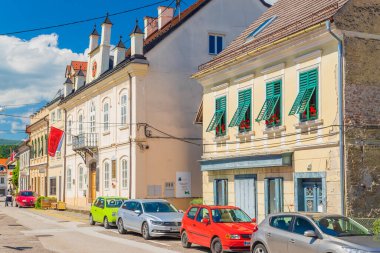 Metlika - 10 Mayıs 2025, Slovenya: Bela Krajina bölgesinde bir kasaba olan Metlika 'nın merkezindeki eski tarihi binanın yakınına park edilmiş modern arabalar.