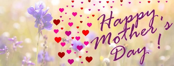 Happy Mother\'s Day written in english in purple with a lot of pink hearts with an image of a flowery field in the background