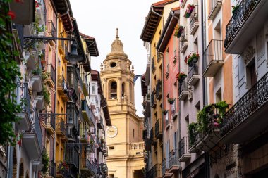 Pamplona, Navarra, İspanya. Pamplona şehrinin güzel sokakları. Çok güzel renkli binalar, farklı renklerde çiçekler, balkonlardan sarkan. Arka planda kilise kulesi 