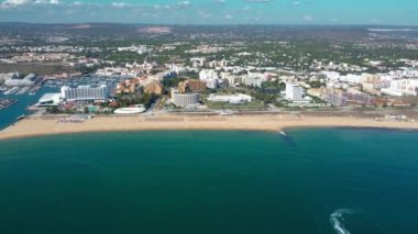 Vilamoura, PORTUGAL: 18 Eylül 2022: Lüks oteller ve kentlerle birlikte Vilamoura sahilinin sinematik hava manzarası. Solda Vilamoura marinası var. İleri ve yavaşça alçalıyor..