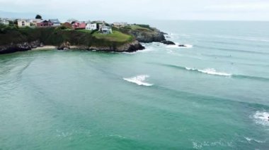 İspanya 'nın kuzeyindeki Asturia' nın güzel hava manzarası. Costal Village Tapia de Casariego manzarası. Evler kayalıklara inşa edilir. Dalgalar kayaları ıslatıyor. Turkuaz su. Sörfçüler. İnsansız hava aracı ilerliyor