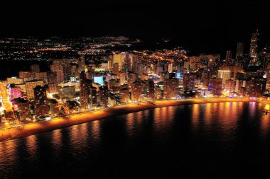 İspanya 'nın Benidorm şehrinin silüeti, geceleri. Sokak lambaları. Suda ışık yansıması. İspanya 'nın güneyinde Alicante eyaletinde muhteşem bir seyahat yeri.  