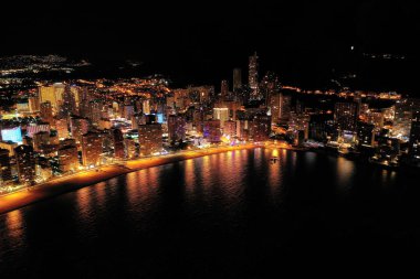 İspanya 'nın Benidorm şehrinin silüeti, geceleri. Sokak lambaları. Suda ışık yansıması. İspanya 'nın güneyinde Alicante eyaletinde muhteşem bir seyahat yeri.  