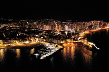 İspanya 'nın Benidorm şehrinin silüeti, geceleri. Sokak lambaları. Suda ışık yansıması. İspanya 'nın güneyinde Alicante eyaletinde muhteşem bir seyahat yeri.  