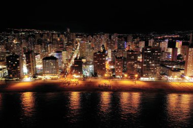 İspanya 'nın Benidorm şehrinin silüeti, geceleri. Sokak lambaları. Suda ışık yansıması. İspanya 'nın güneyinde Alicante eyaletinde muhteşem bir seyahat yeri.  