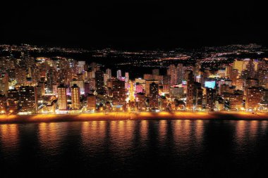 İspanya 'nın Benidorm şehrinin silüeti, geceleri. Sokak lambaları. Suda ışık yansıması. İspanya 'nın güneyinde Alicante eyaletinde muhteşem bir seyahat yeri.  