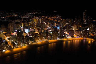 İspanya 'nın Benidorm şehrinin silüeti, geceleri. Sokak lambaları. Suda ışık yansıması. İspanya 'nın güneyinde Alicante eyaletinde muhteşem bir seyahat yeri.  