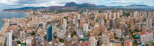 stock image Aerial drone point of view of Benidorm city. Famous travel destination in Alicante province, Spain. Skyscrapers, mountains in background, Mediterranean Sea. Cloudy day. 