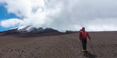 Genç dağcı, bulutlu bir günde Cotopaxi yanardağının kumsalında tek başına yürüyüş direkleriyle yürüyor.