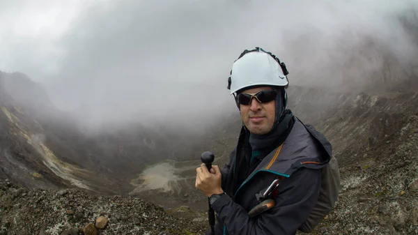 Genç dağcı, bulutlu bir günde, Guagua Pichincha volkanının yanında tek başına yürüyüş direğini kullanarak siyah ceketli ve kasklı yürüyor.