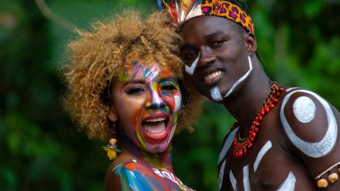 Nueva Loja, Sucumbios / Ekvador - 3 Eylül 2020: Odaklanmamış yeşil arka planı olan bir ormanda renkli yüzleri olan genç siyah bir çiftin portresi