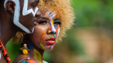 Nueva Loja, Sucumbios / Ekvador - 3 Eylül 2020: Odaklanmamış yeşil arka plana sahip bir ormanda renkli yüzlü, ciddi bir ifadeye sahip genç siyah bir çiftin profil portresi