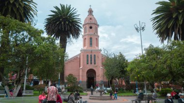 Otavalo, Imbabura / Ekvador - 14 Ekim 2023: İnsanlar arka plandaki ağaçların arasında katedralle birlikte Otavalo 'nun merkez parkında yürüyor