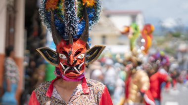Pillaro, Tungurahua / Ekvador - 5 Ocak 2024: Pillaro şehrindeki Diablada Pillarena geçit töreninde arka planda dans eden şeytanlarla ön planda kırmızı şeytan gibi giyinmiş adam - Ekvador