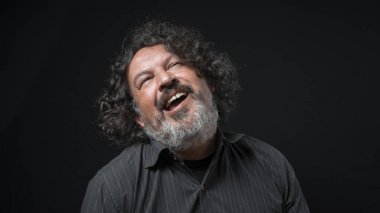 Beyaz sakallı, siyah kıvırcık saçlı siyah saçlı, siyah arka planda siyah gömlekli bir adamın portresi.