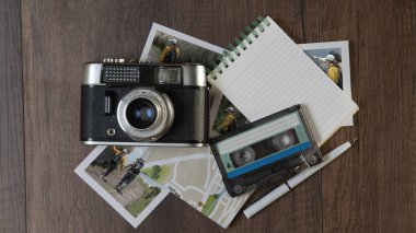 Eski fotoğraf makinesinin üst görüntüsü farklı yerlerde çekilmiş fotoğraflarla çevrili. Harita, defter ve müzik kaseti.