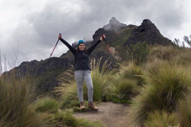 Siyah kazaklı güzel bir kadın bulutlu bir günde çalılığın ortasındaki toprak yolda zafer işareti yapıyor.